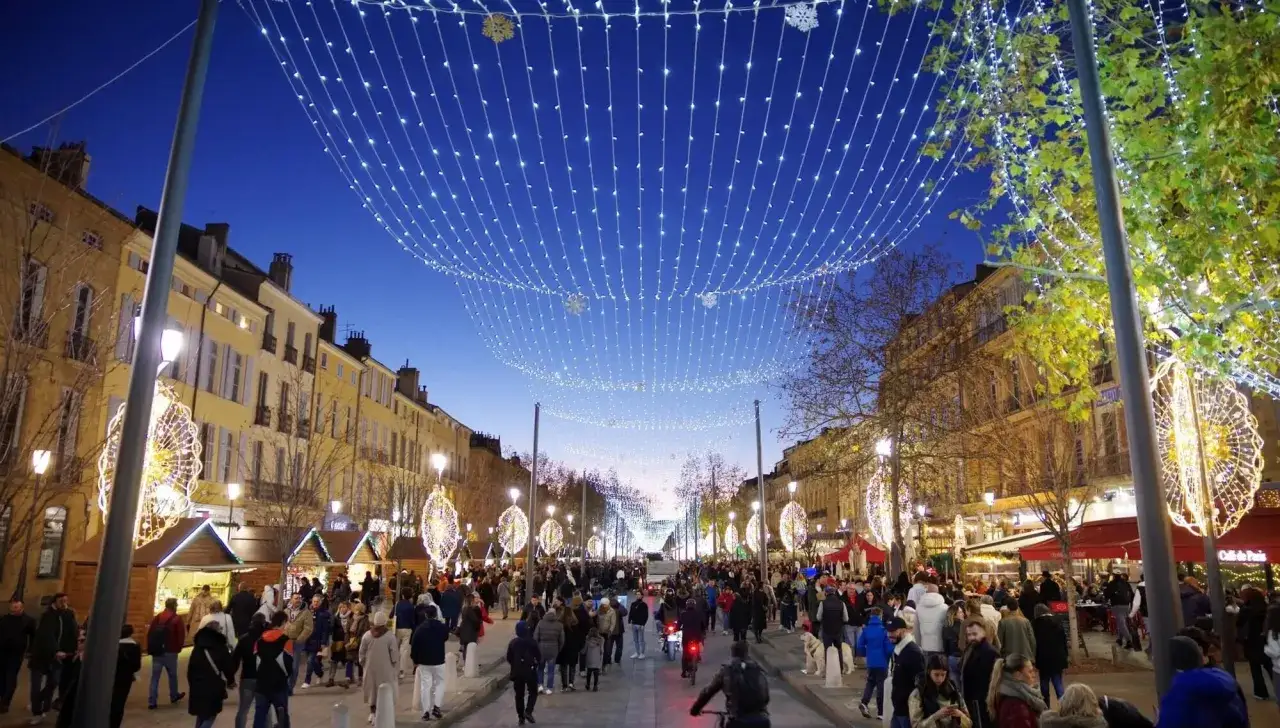 Foule joyeuse au marché de noël Vaucluse, illuminé par des guirlandes scintillantes et des décorations festives.