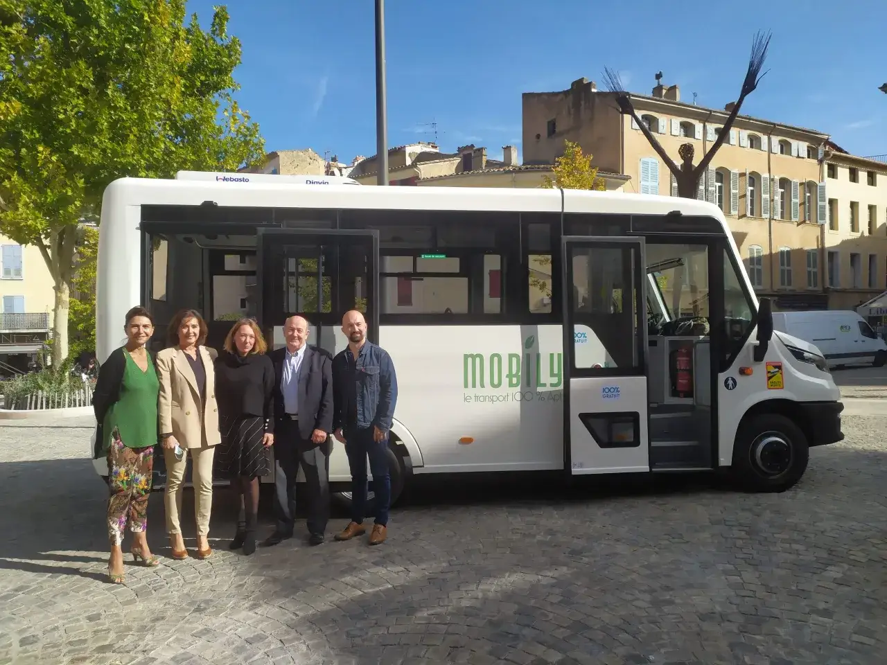 Cinq personnes posent devant un bus blanc 