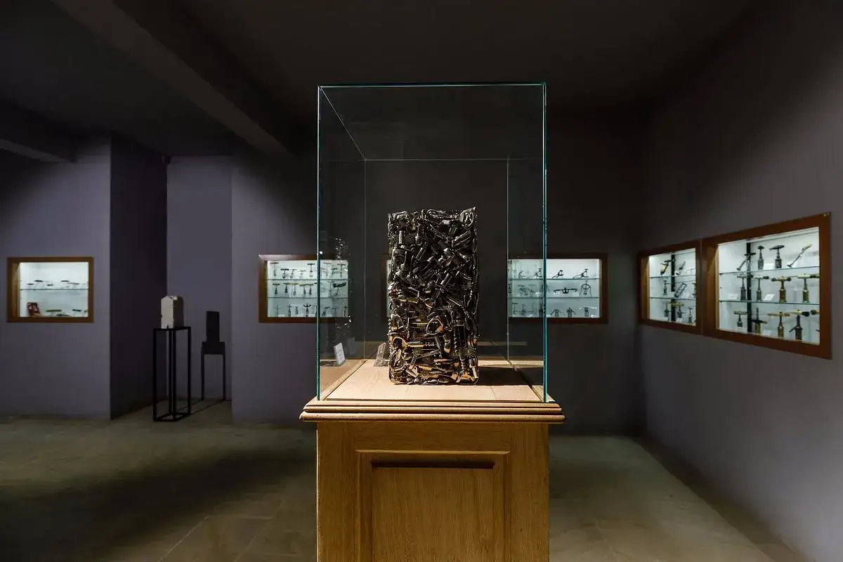 Sculpture d'outils anciens dans une vitrine au musée du tire bouchon. Des étagères murales exposent des tire-bouchons variés.