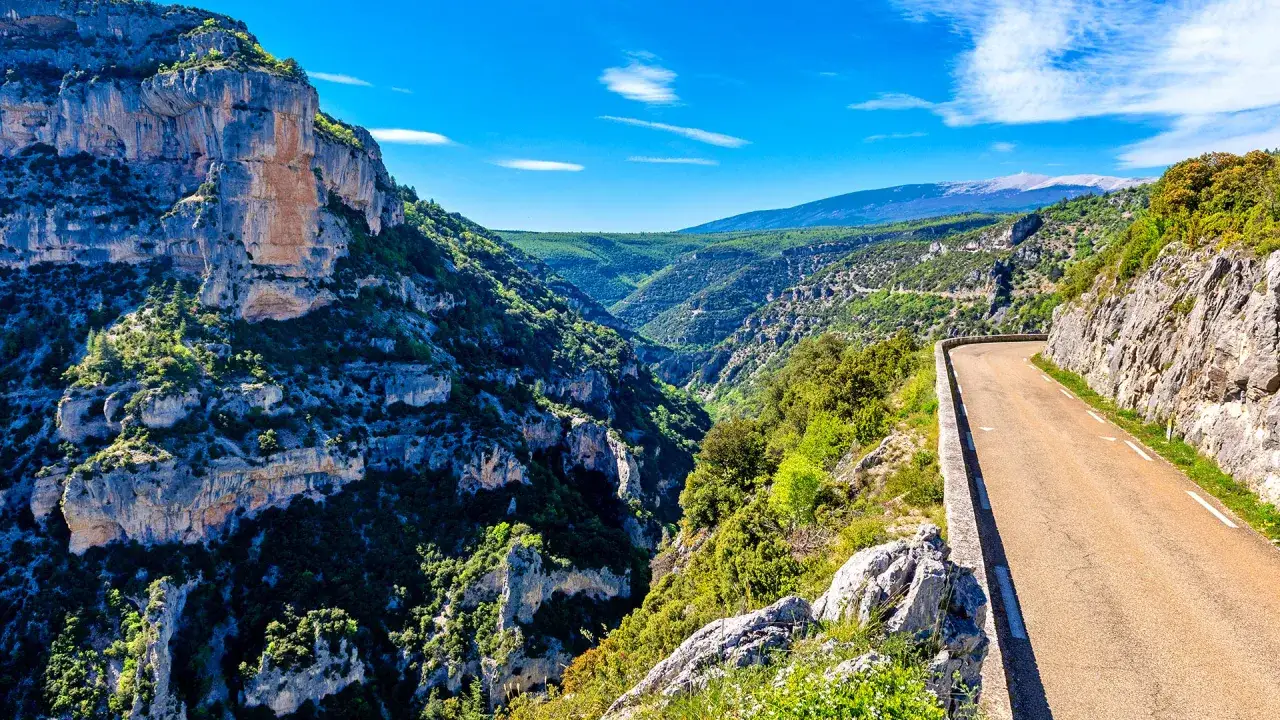 Route sinueuse traversant les gorges de la Nesque, offrant des vues spectaculaires sur les falaises et la vall&eacute;e verdoyante.