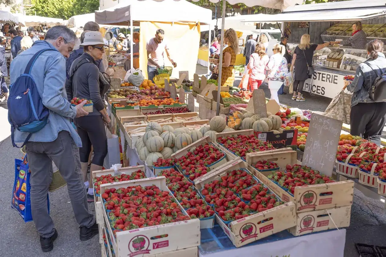 Le marché de Forcalquier est animé. Des étals débordent de fruits et légumes frais, notamment de magnifiques fraises en caisses.