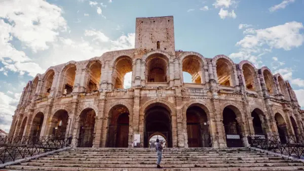 Visiter Arles : une personne tient un bébé sur les marches de l'amphithéâtre romain, sous un ciel bleu et nuageux.