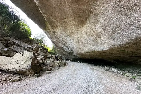 Le chemin menant au fort de Buoux serpente sous un immense surplomb rocheux, offrant un aperçu de la nature sauvage.