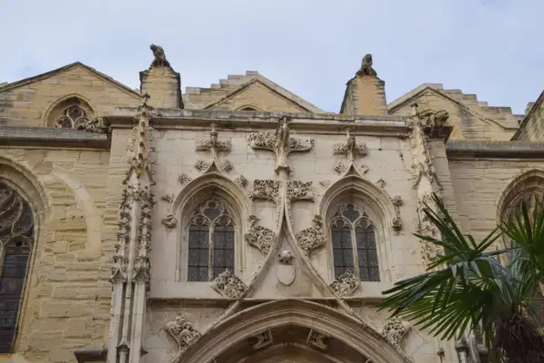 Détail architectural d'une cathédrale, un joyau du tourisme à Carpentras. Gargouilles et fenêtres gothiques sous un ciel couvert.
