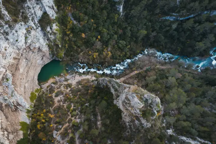 Vue aérienne de la Fontaine de Vaucluse, avec son bassin émeraude et la rivière Sorgue serpentant à travers une gorge boisée.
